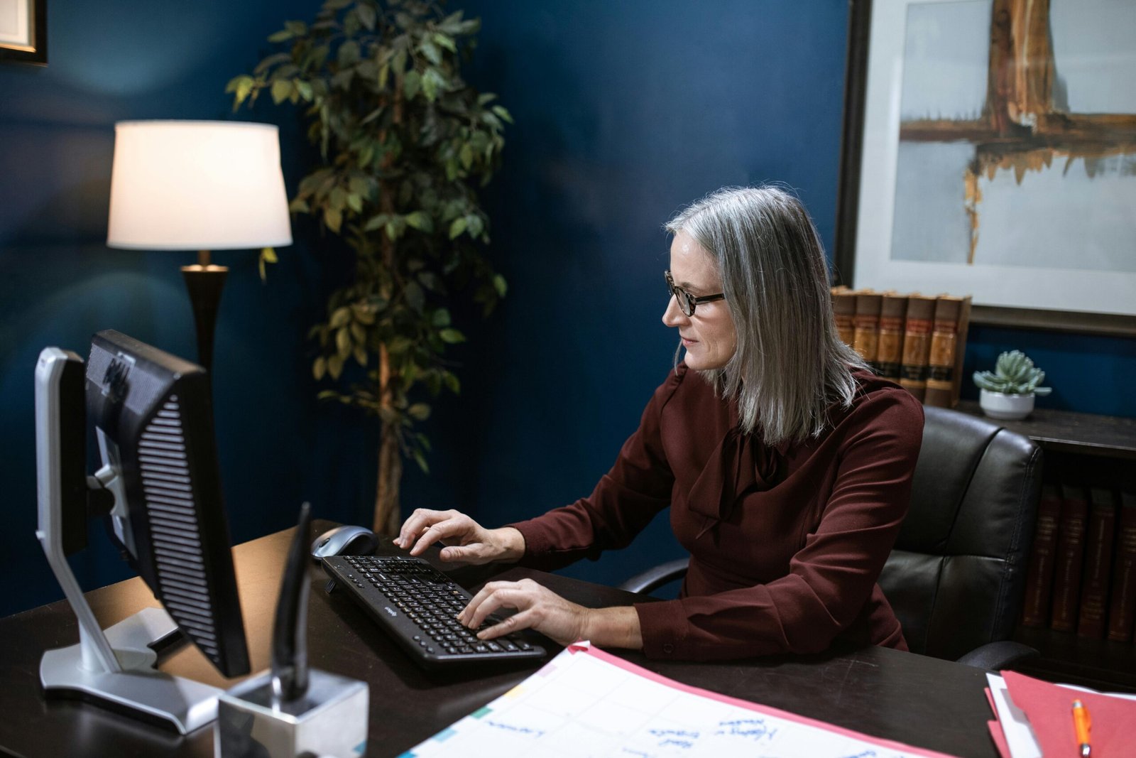 Mature woman in a modern office typing on a keyboard, focused and professional.